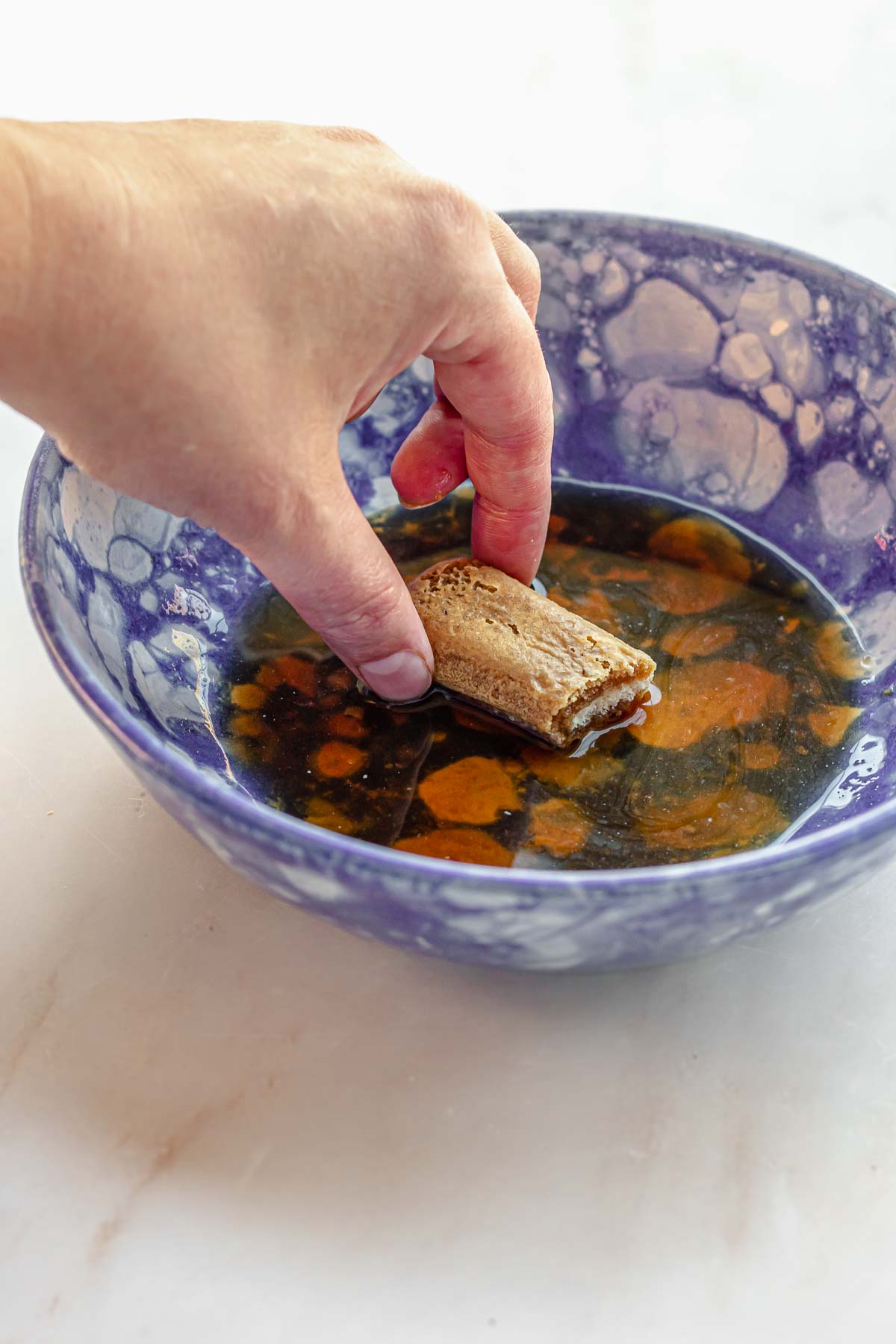 A hand soaks a piece of ladyfingers in coffee in a bowl.