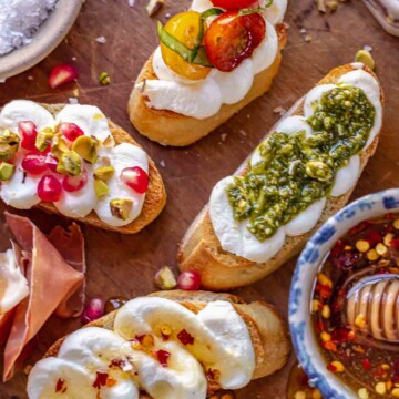 An arrangement of whipped ricotta crostini on a board with fixings.