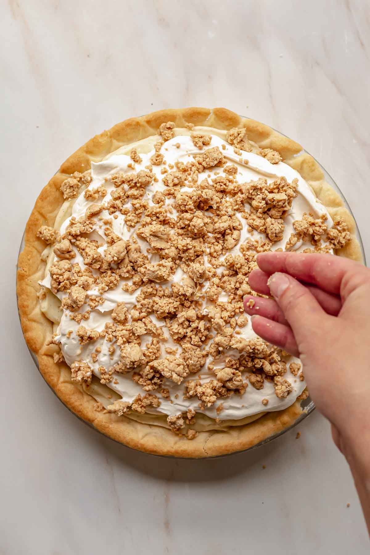 A hand sprinkles peanut butter crumbles top of whipped cream.