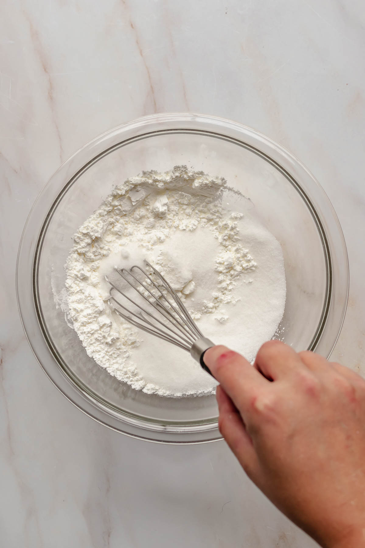 A hand whisks sugar and corn starch in a bowl.