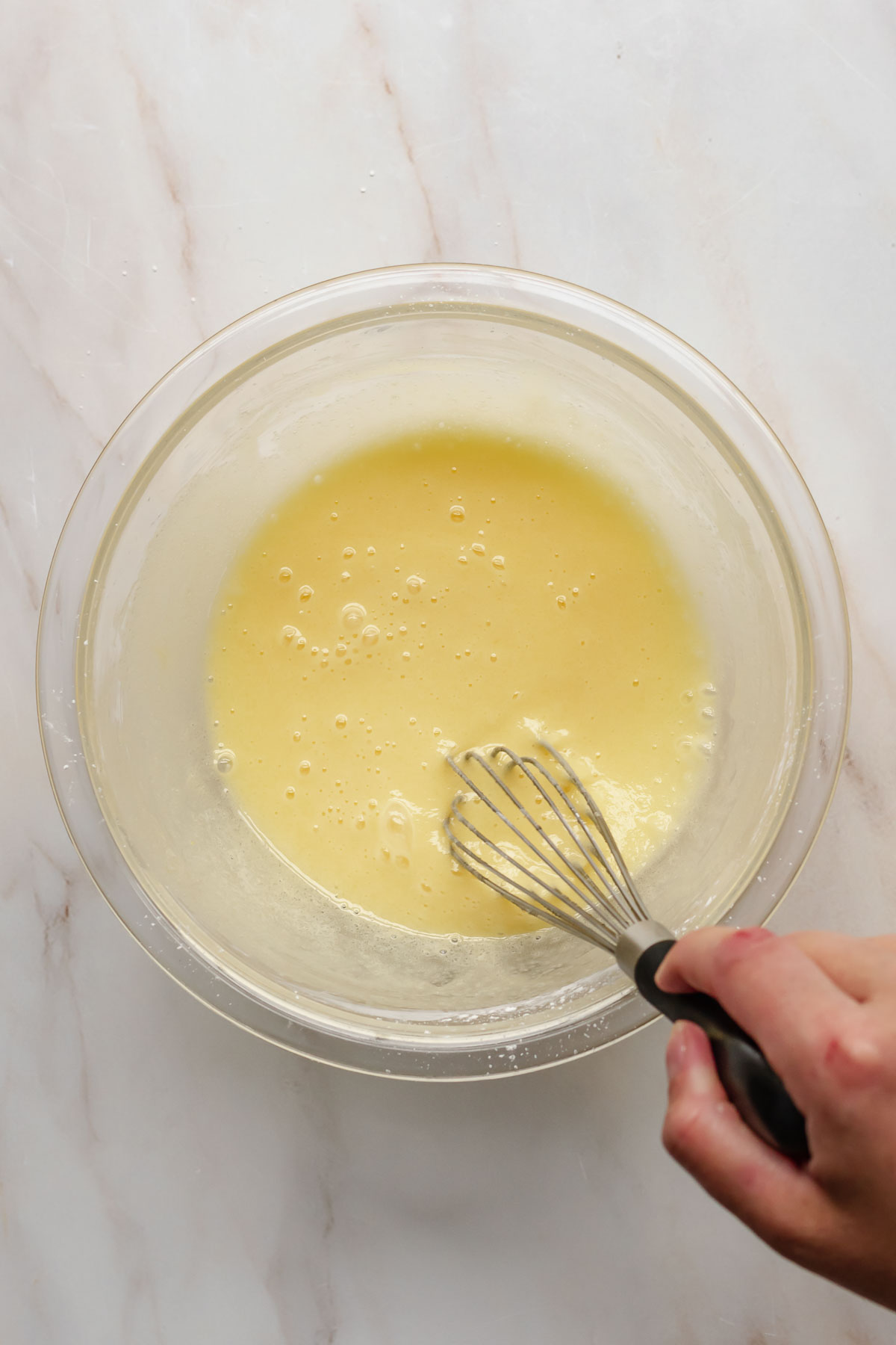 A hand whisks egg yolks and sugar in a bowl.