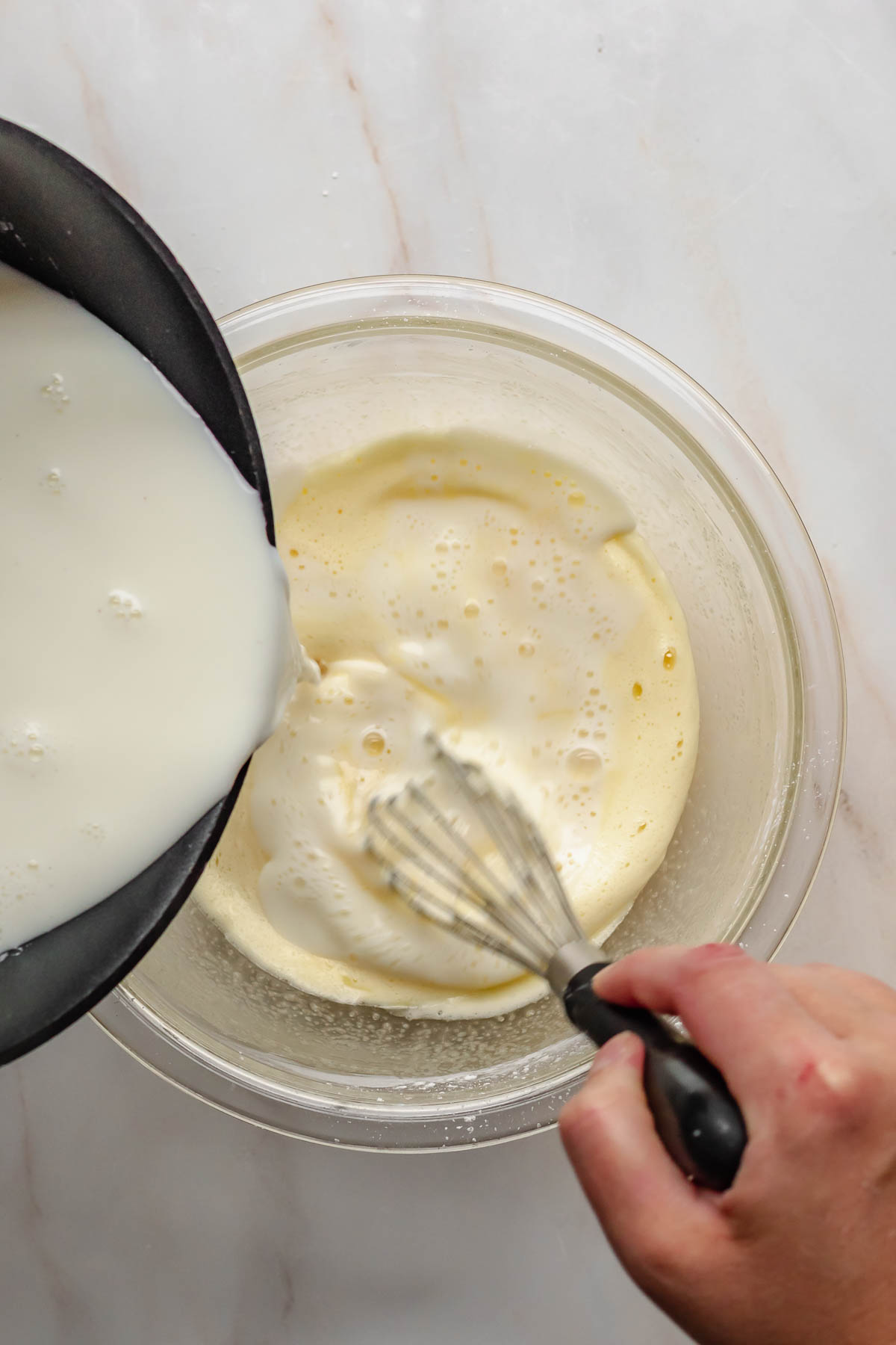 Pouring hot cream into egg yolks while whisking.