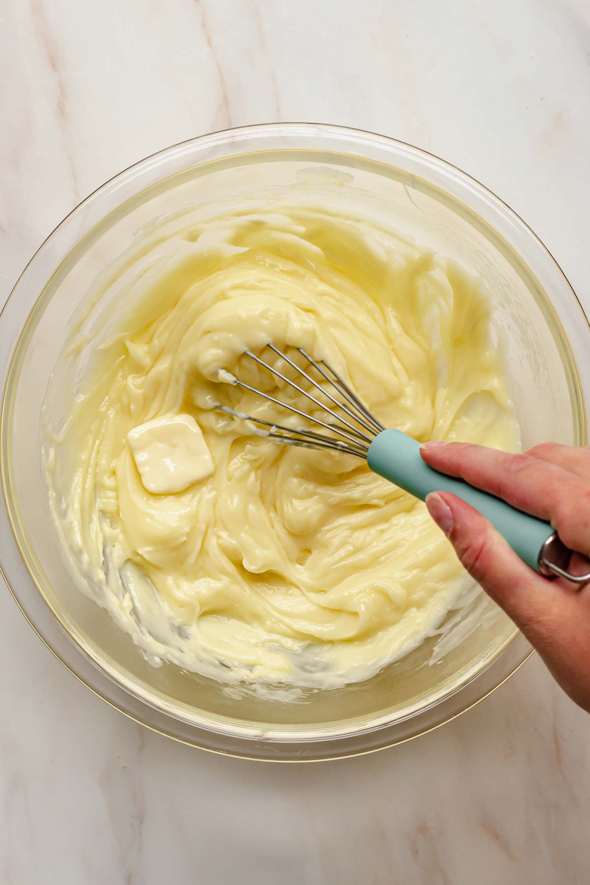 A hand whisks butter into vanilla pudding.