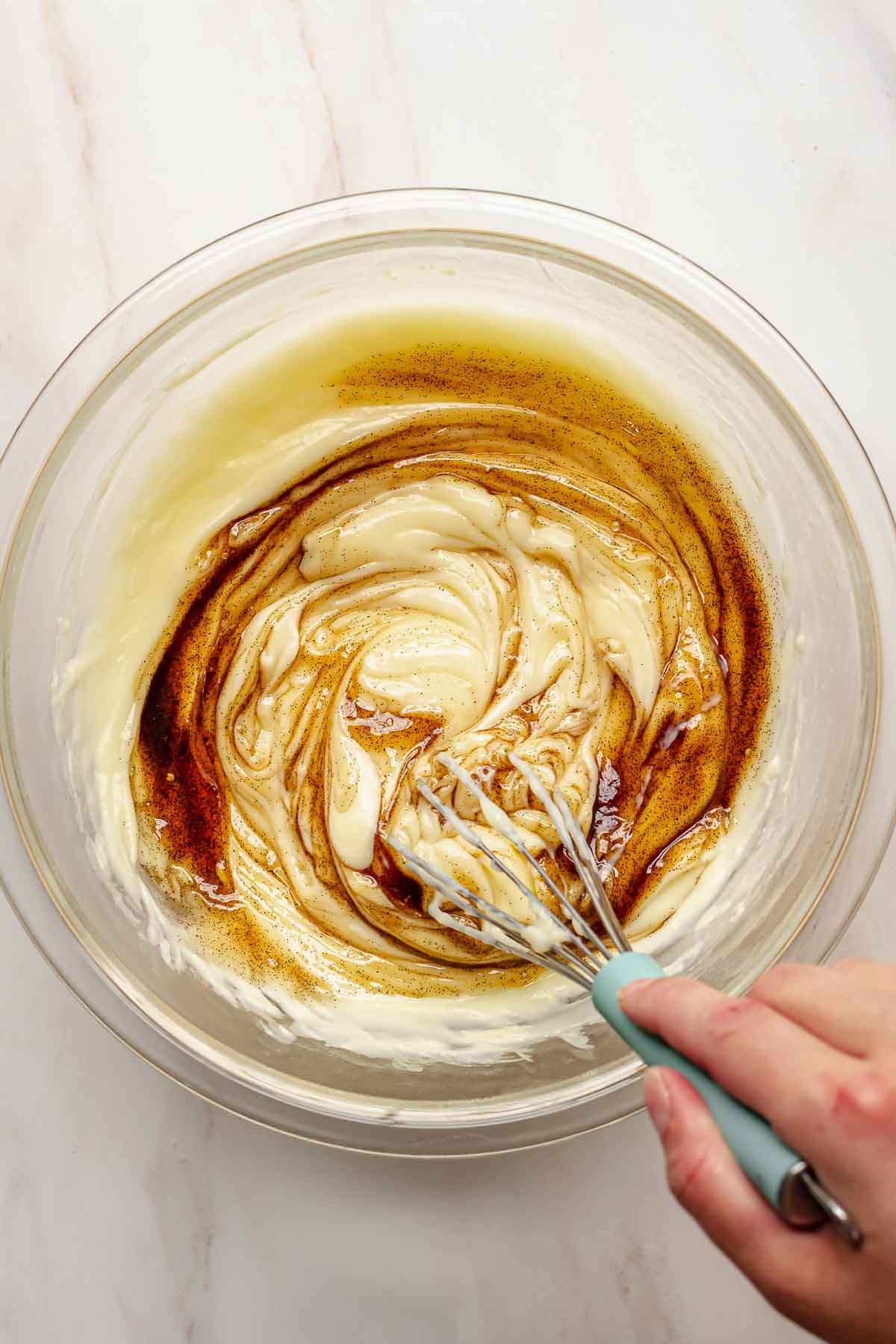 A hand whisks vanilla paste into vanilla pudding.
