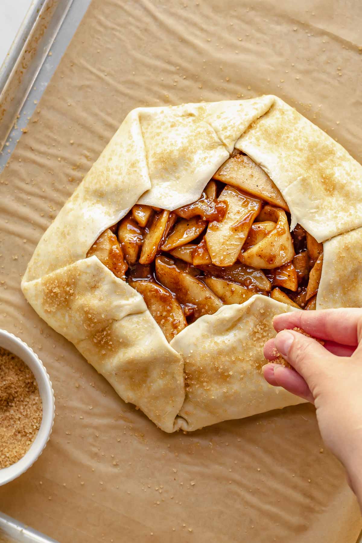 A hand sprinkles coarse sugar on the pie crust before baking.