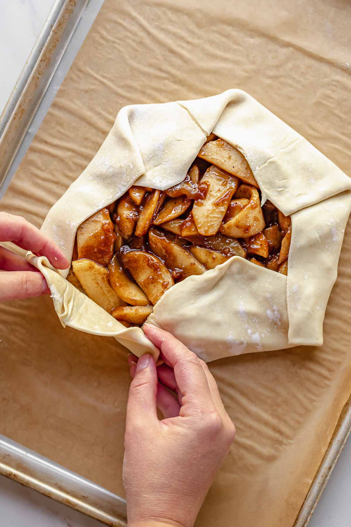 Hands fold the puff pastry upwards over the apples.