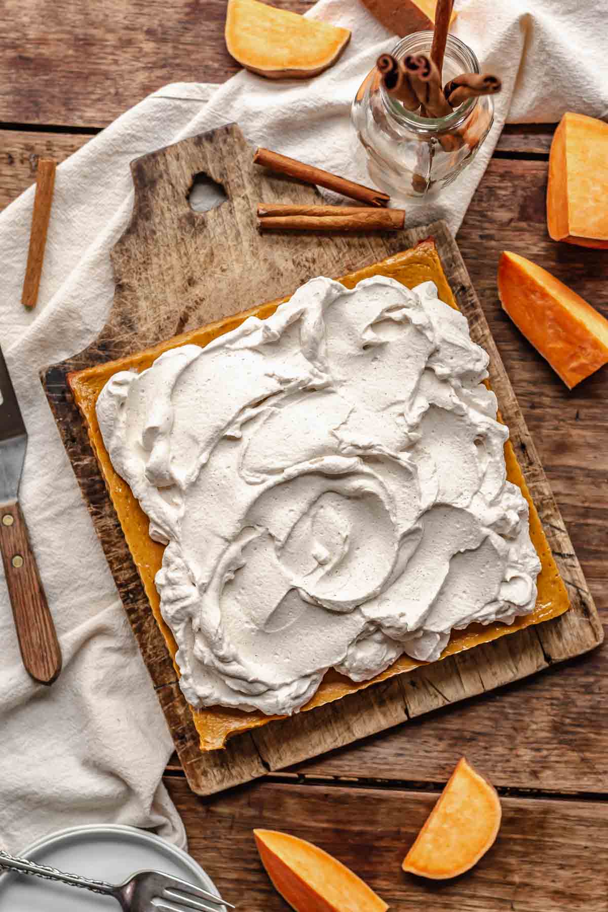 Cinnamon whipped cream swooped onto uncut sweet potato bars on a cutting board.
