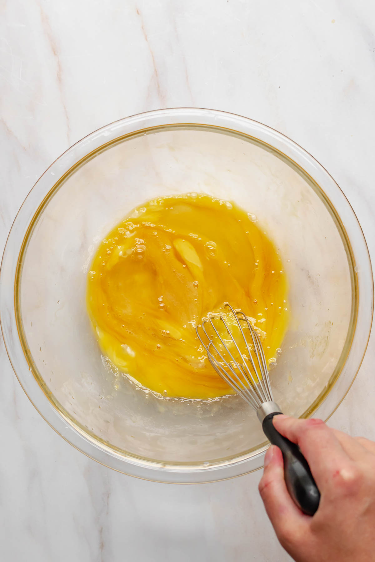 A hand whisks together eggs in a bowl.