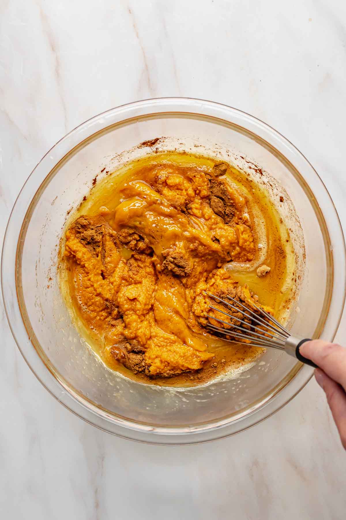 A hand whisks together sweet potato pie filling in a bowl.
