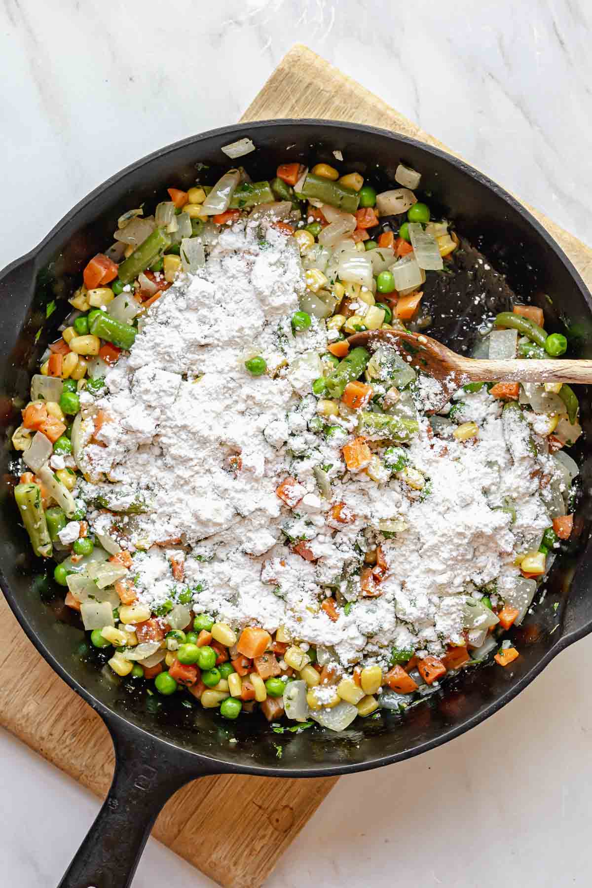Flour sprinkled over mixed vegetables in a pan.