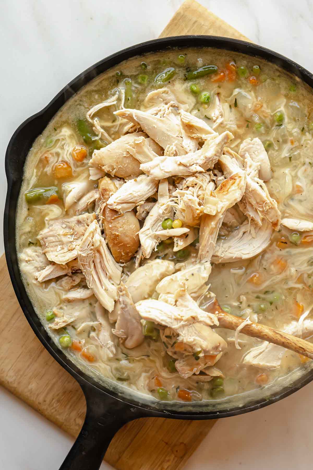 A spoon stirs shredded turkey into the pot pie filling.