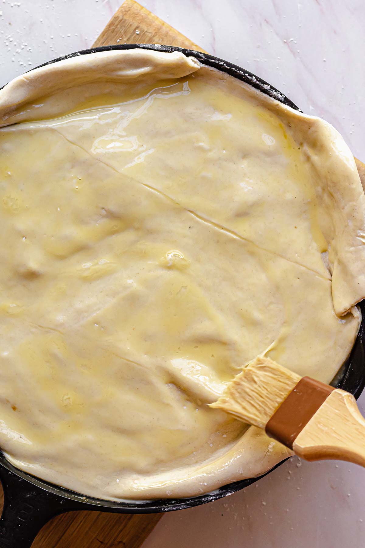 A brush swipes whisked egg on top of puff pastry.