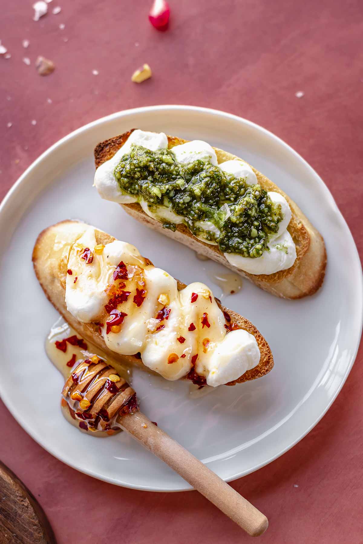 Two crostinis on a plate, one topped with hot honey and one topped with pesto.