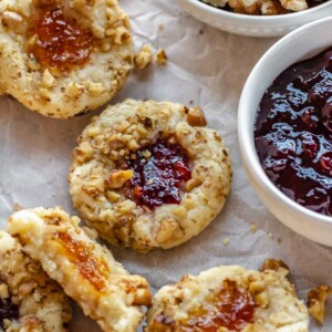 Thumbprint cookies scattered around a bowl of jam.