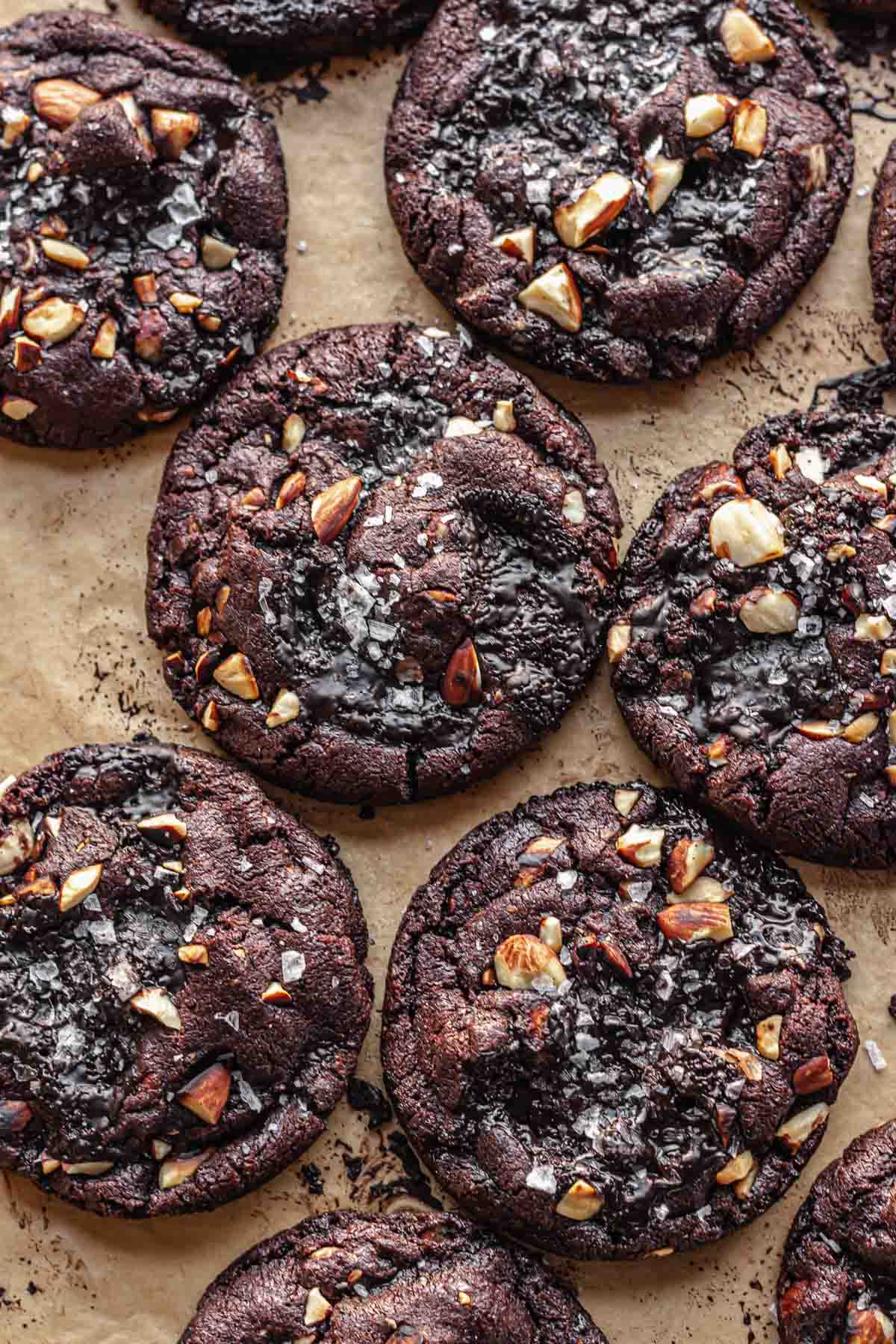 Baked chocolate almond cookies on a cookie sheet touching each other.