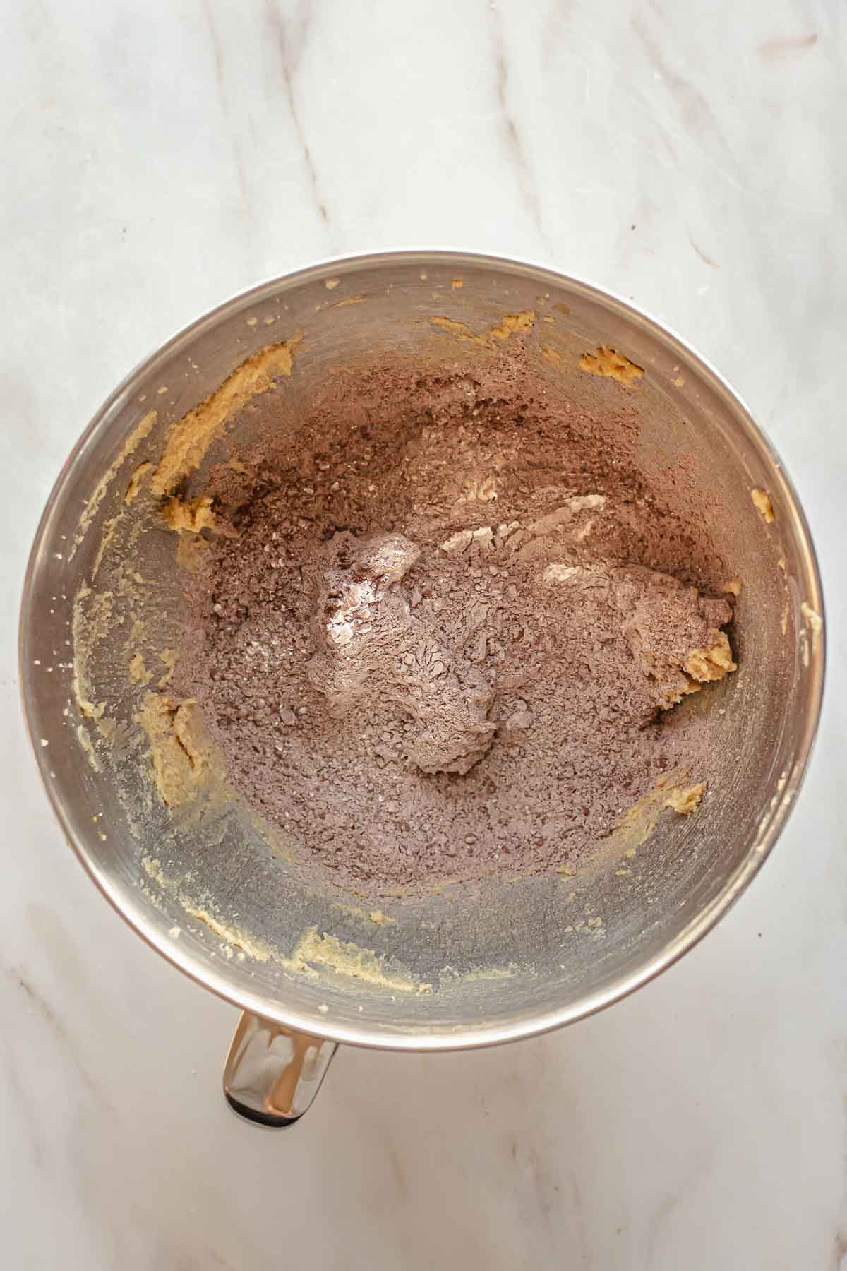 Cocoa powder and flour on top of creamed butter and sugar in a bowl.