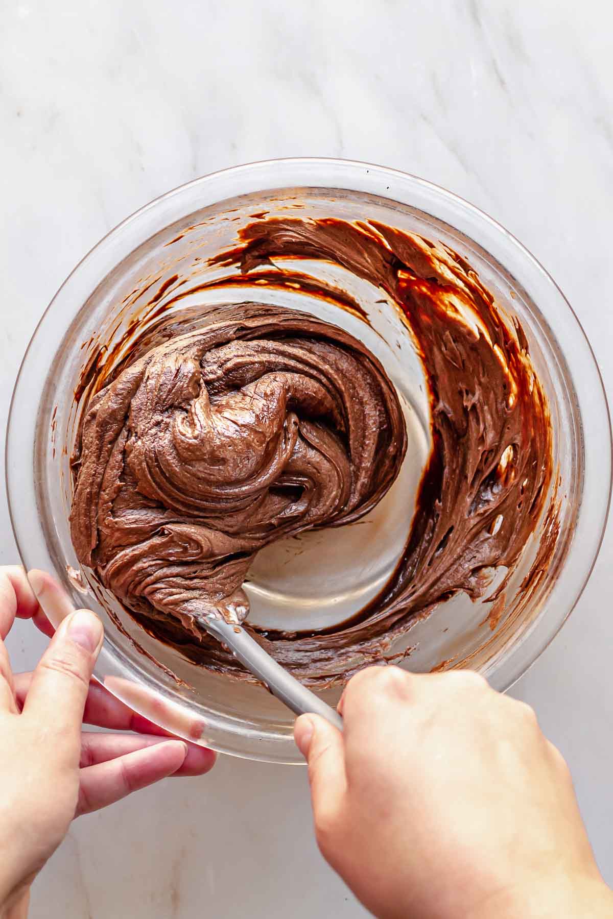 A hand mixes chocolate into cream cheese frosting.