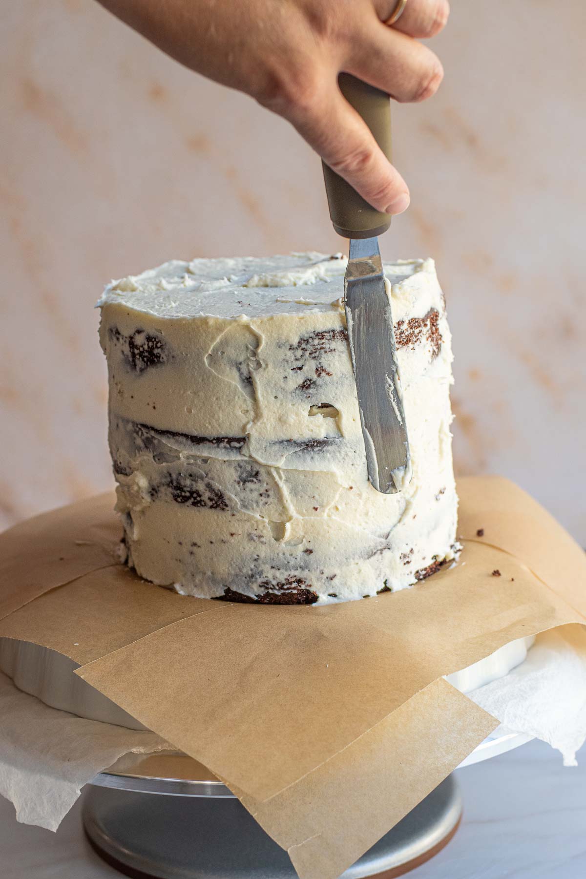 A hand spreads cream cheese frosting to cover the assembled cake.