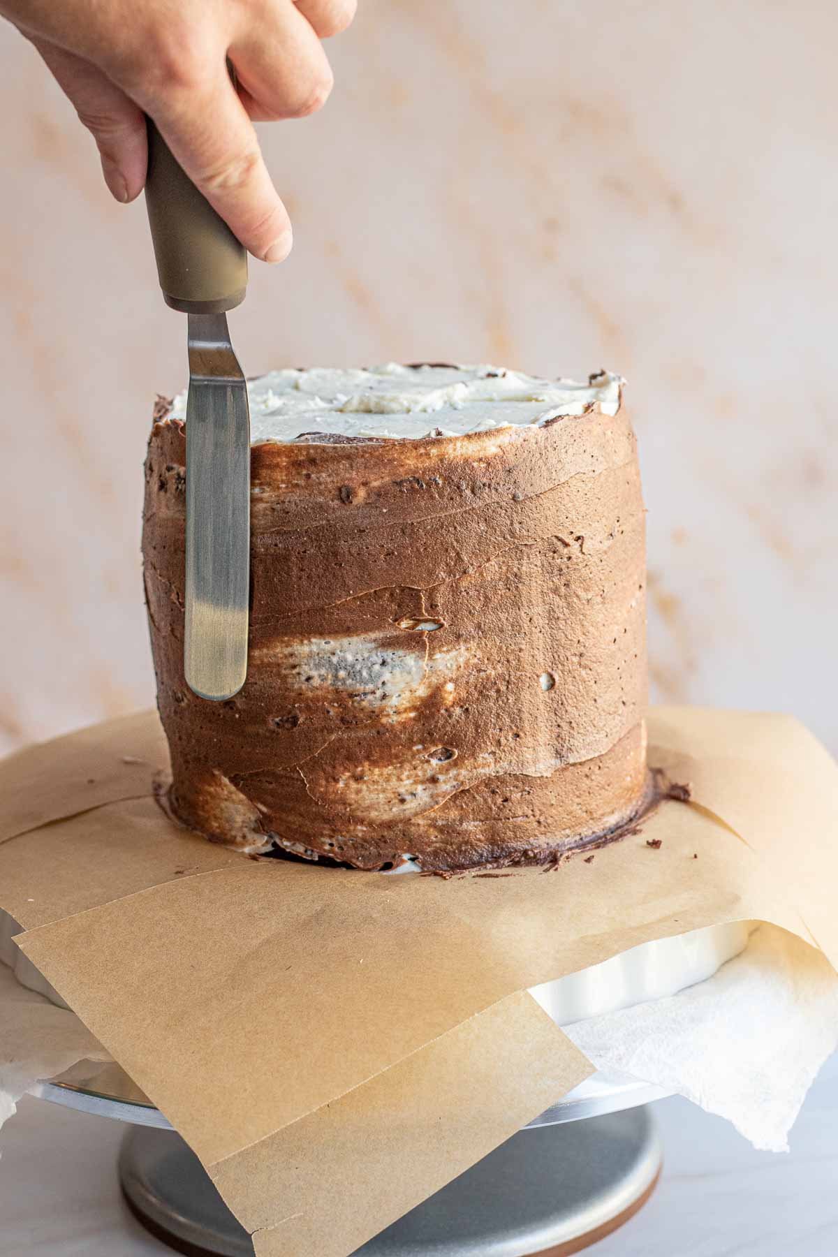 A spatula spreads chocolate cream cheese frosting through the vanilla.