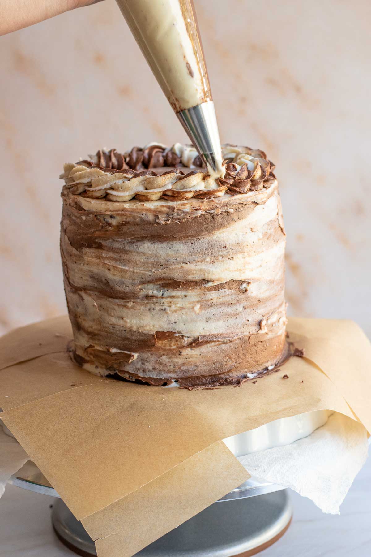 A piping tip pipes swirls onto the top of the frosted cake.