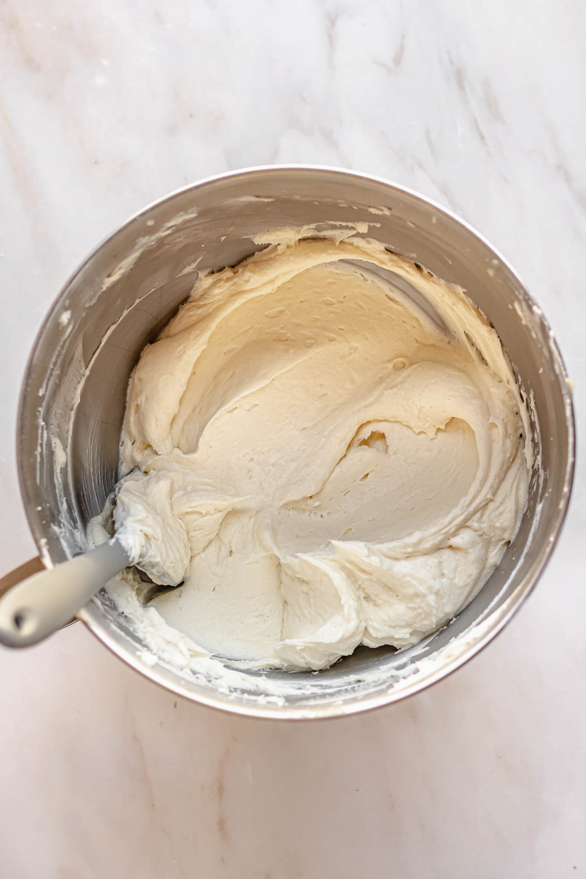 Smooth cream cheese frosting in a bowl with a spatula in the bowl.