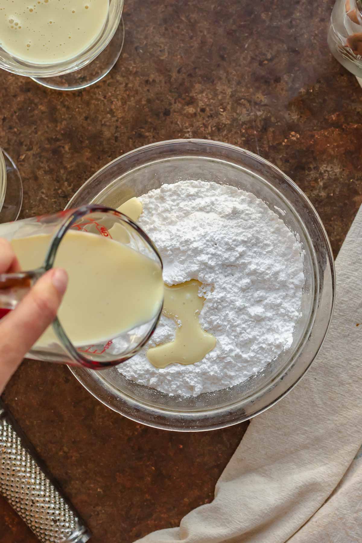Eggnog being poured into a bowl of powdered sugar.