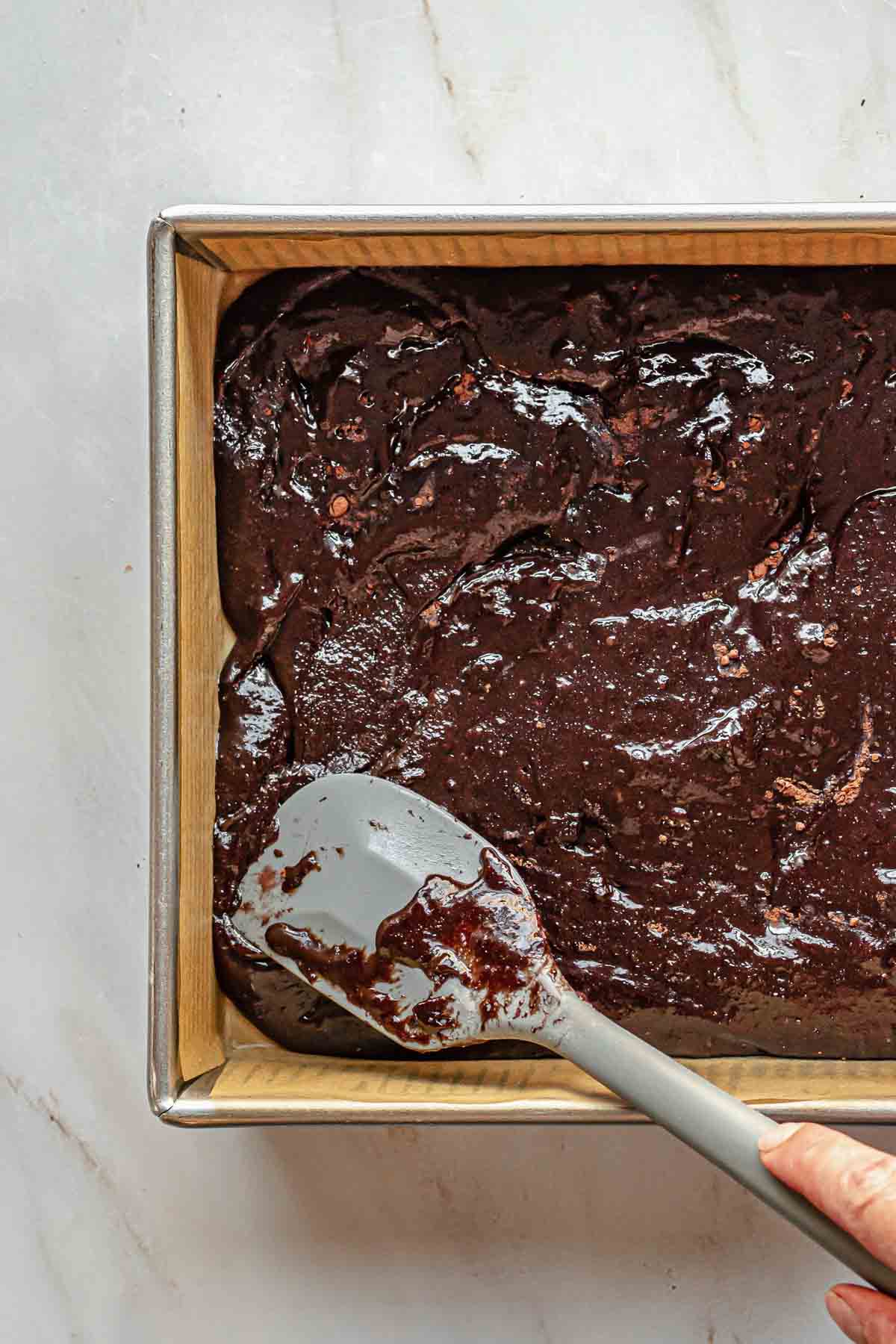 A spatula spreads the brownie batter to the edges of the pan.