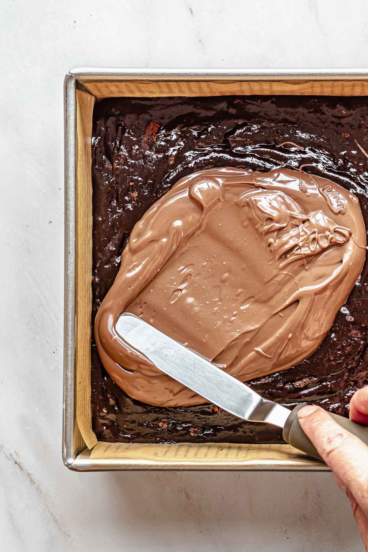 A spatula spreads Nutella on top of brownie batter.