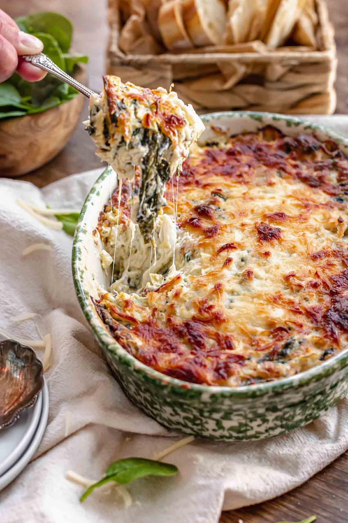 A spoon pulls out a cheesy bite of hot crab spinach dip.
