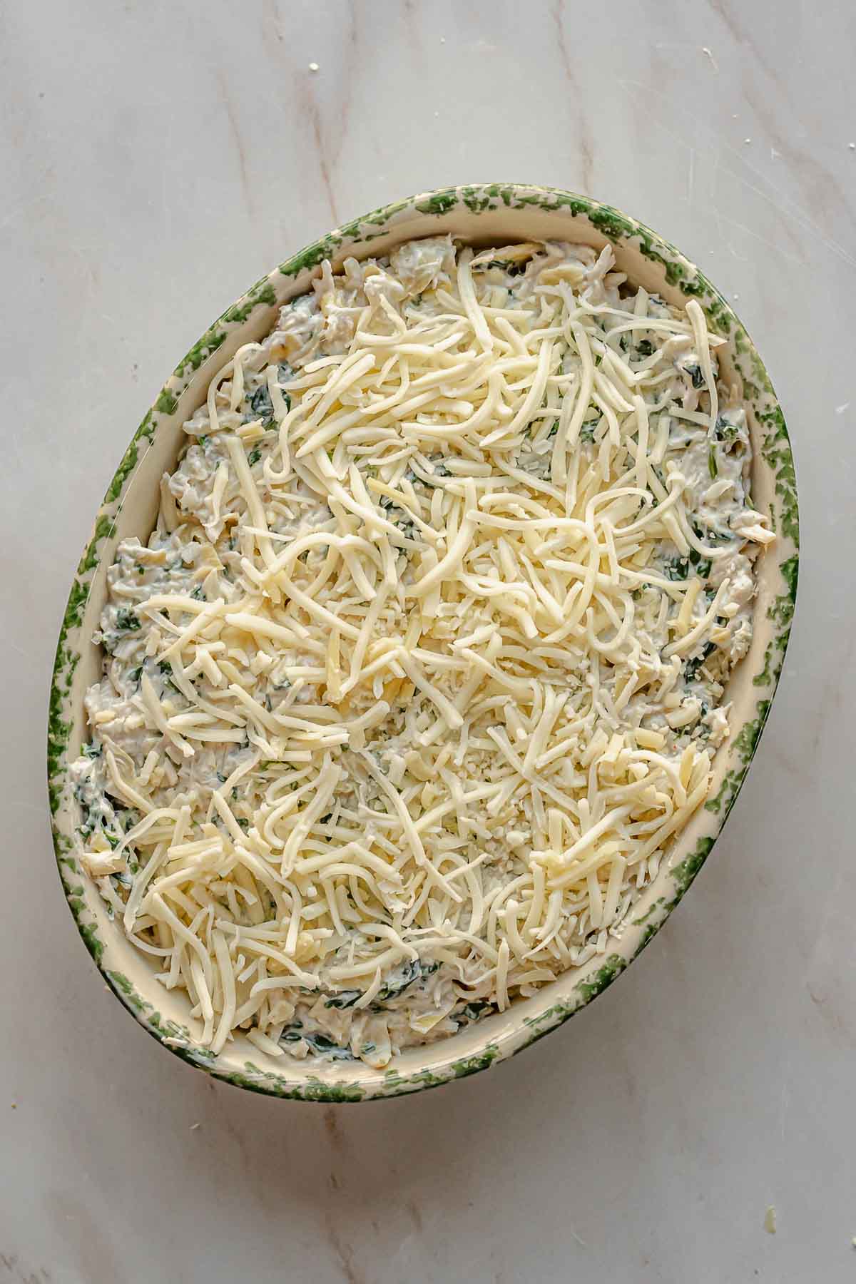 Shredded cheese sits on top of crab spinach dip prior to baking.