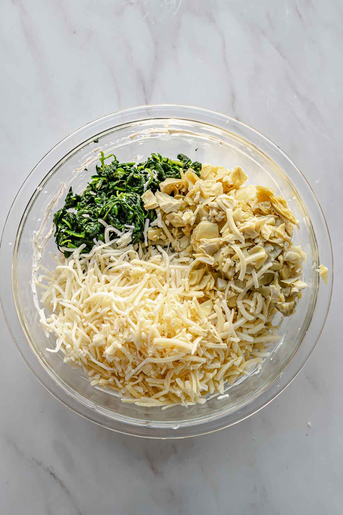 Cheeses, chopped artichokes, and chopped spinach in a bowl.