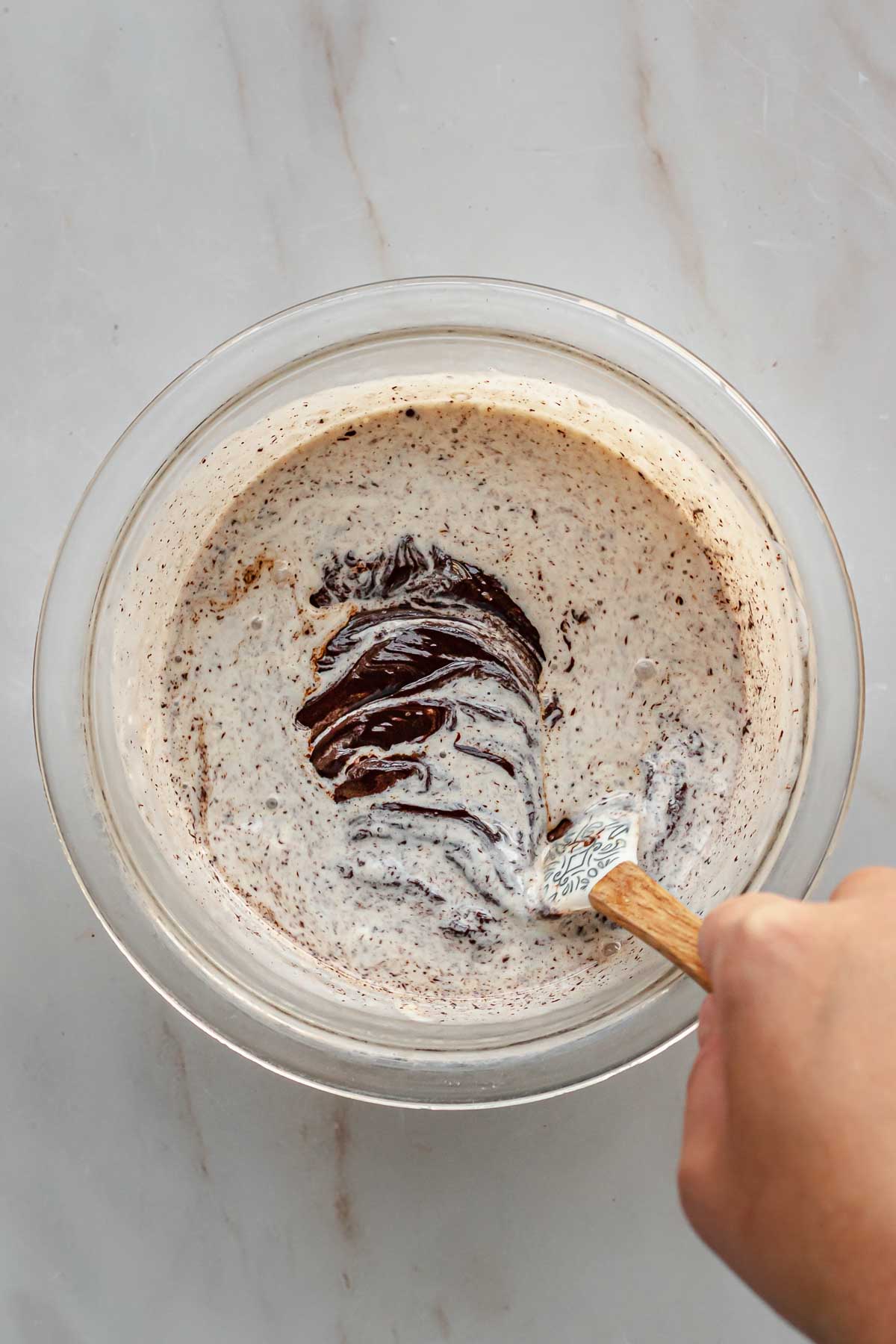 A hand stirs together chocolate and heavy cream in a bowl.