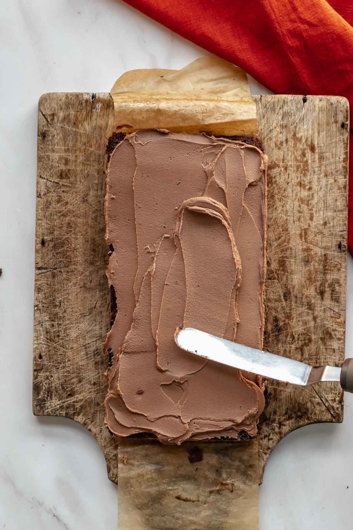 A spatula spreads milk chocolate ganache onto a layer of cake.