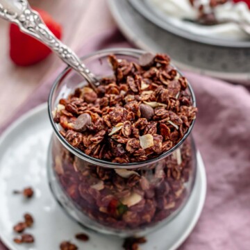 Chocolate granola in a cup with a spoon in it.
