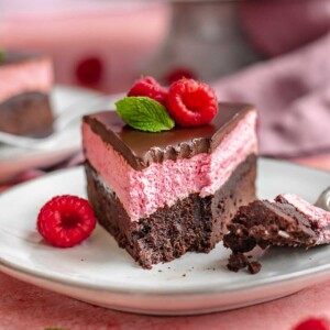 Piece of chocolate raspberry cake on a plate with a bite removed.