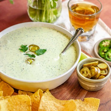 Jalapeno ranch dip in a bowl with chips and jalapeños on the side.