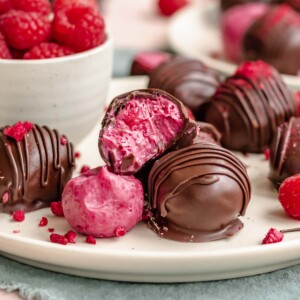 Raspberry truffles stacked on plate. One has a bite removed.