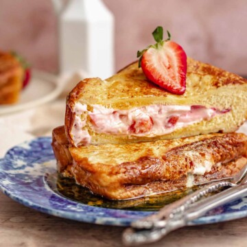 Two stacks of strawberry stuffed French toast on a plate. One is cut in half to show the insides.