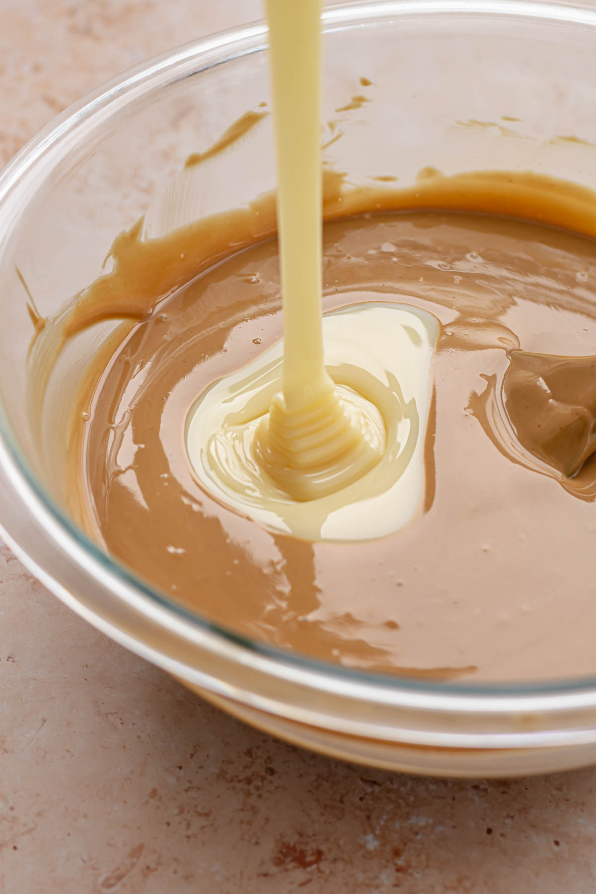 Sweetened condensed milk pouring into a bowl of white chocolate and cookie butter.