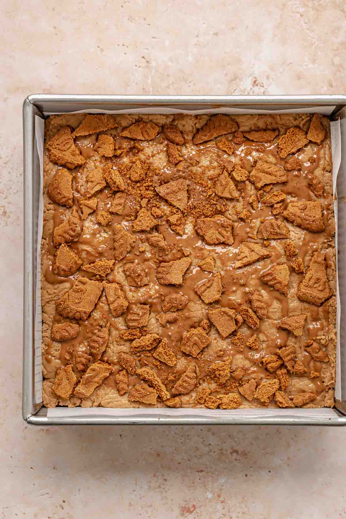 Biscoff fudge in a pan with crushed cookies on top.