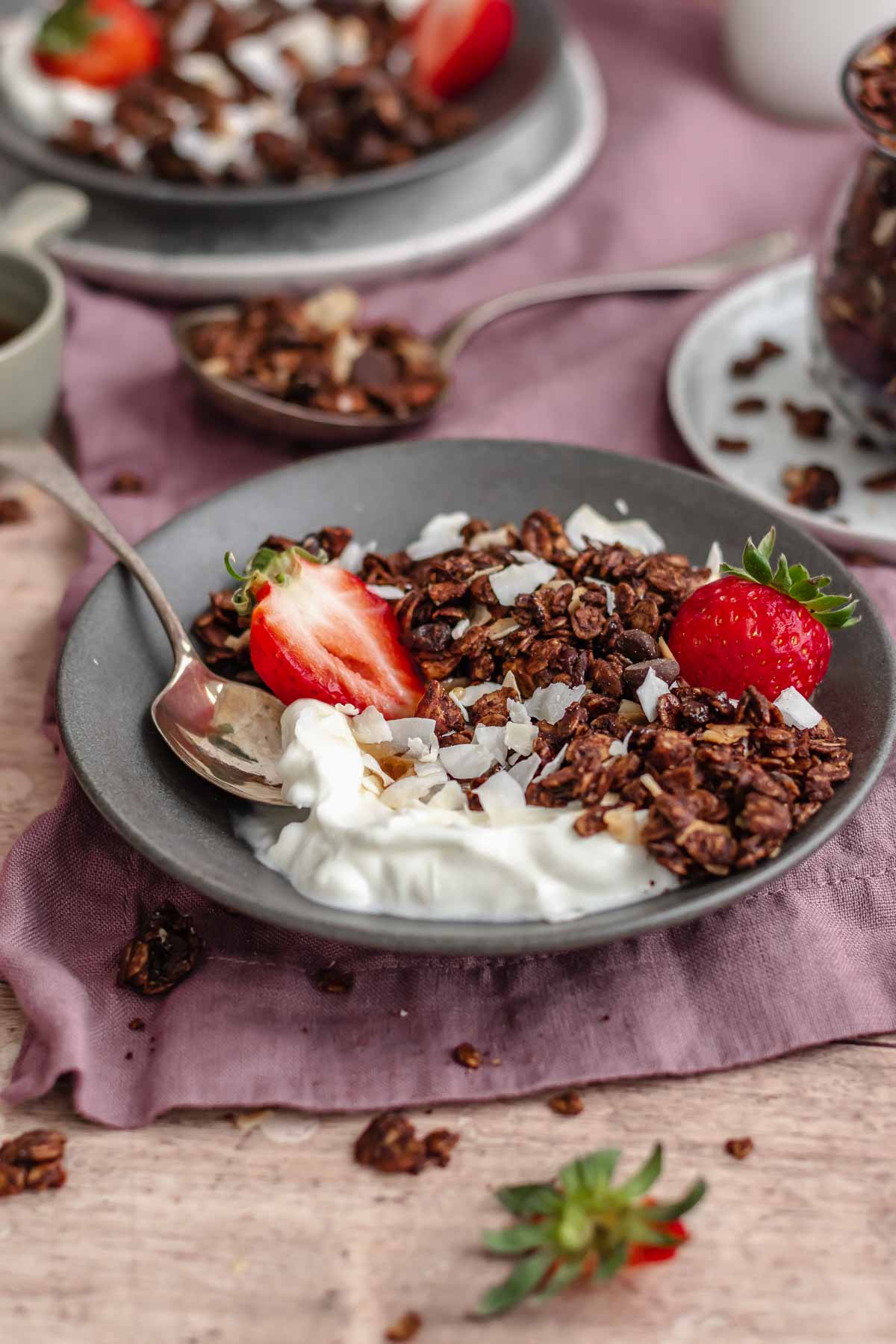Granola and yogurt in a bowl with a spoon and strawberries.
