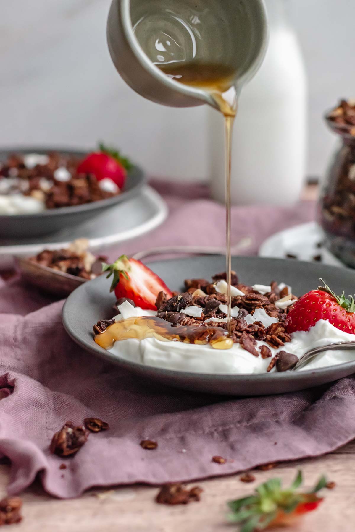 Maple syrup pouring over yogurt and chocolate granola in a bowl.