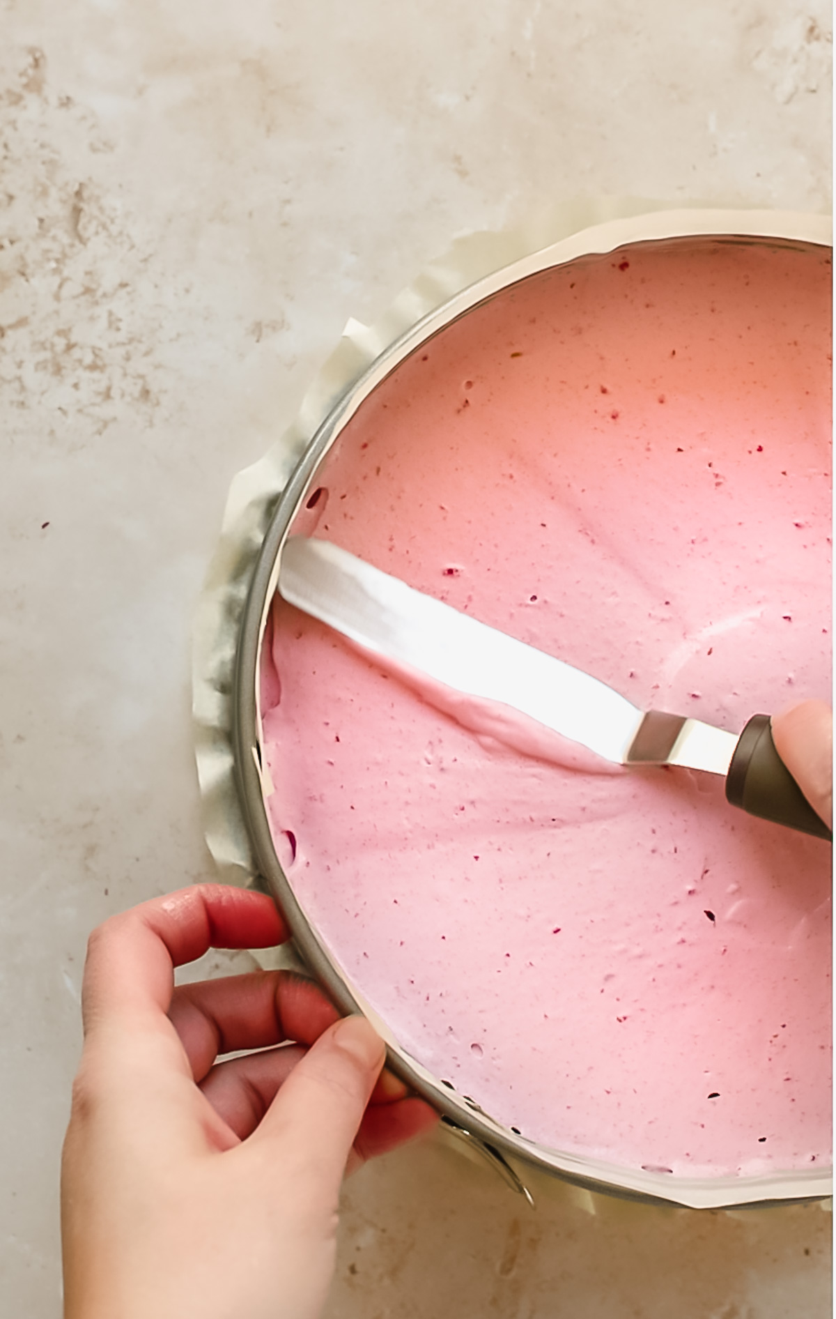 A spatula smooths raspberry mousse on the chocolate cake.