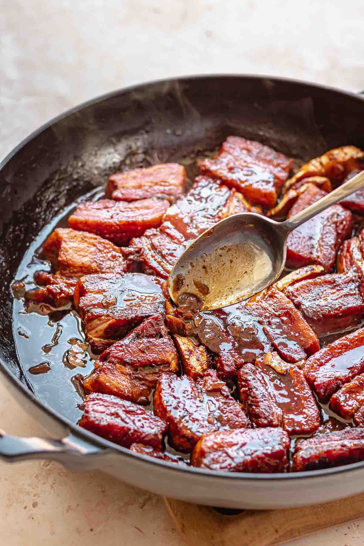 A spoon pours braising liquid on top of cooked pork belly.