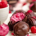 Raspberry truffles stacked on plate. One has a bite removed.