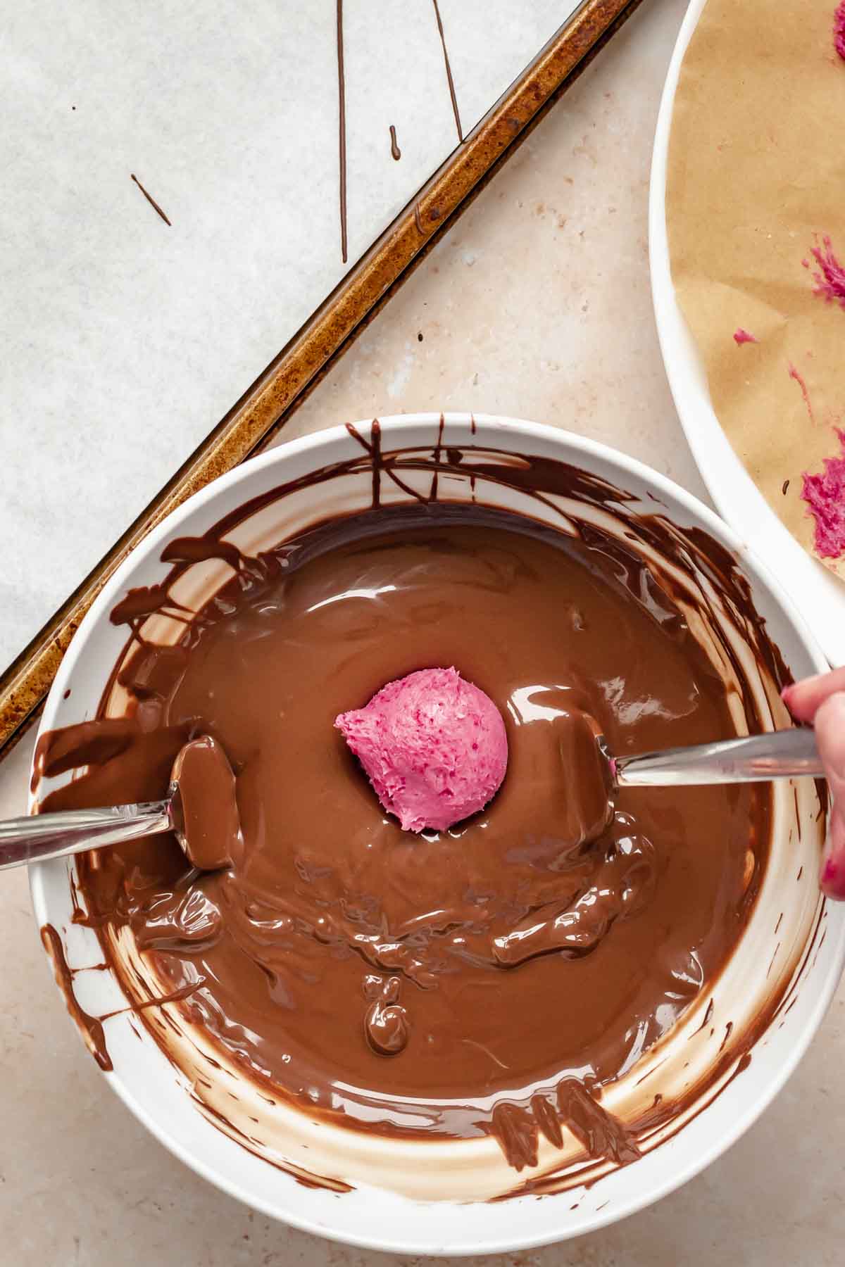 A truffle in a bowl of melted chocolate with two forks underneath.