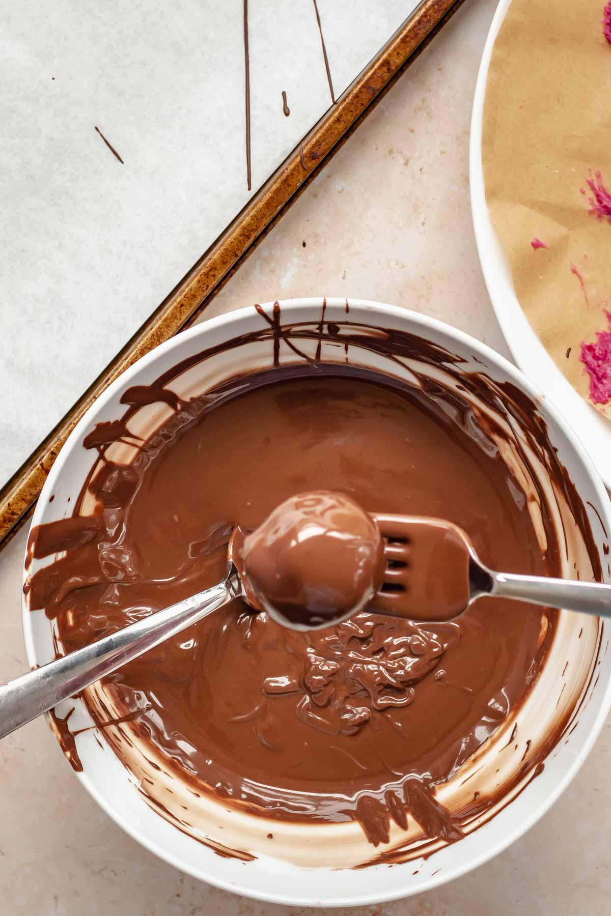 Two forks hold up a chocolate covered truffle.