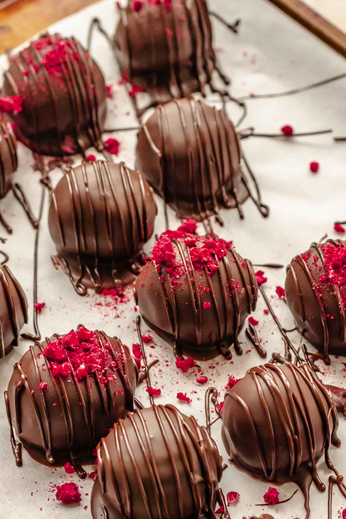 Chocolate raspberry truffles on a sheet pan. Some have freeze dried raspberry crumbles on top.