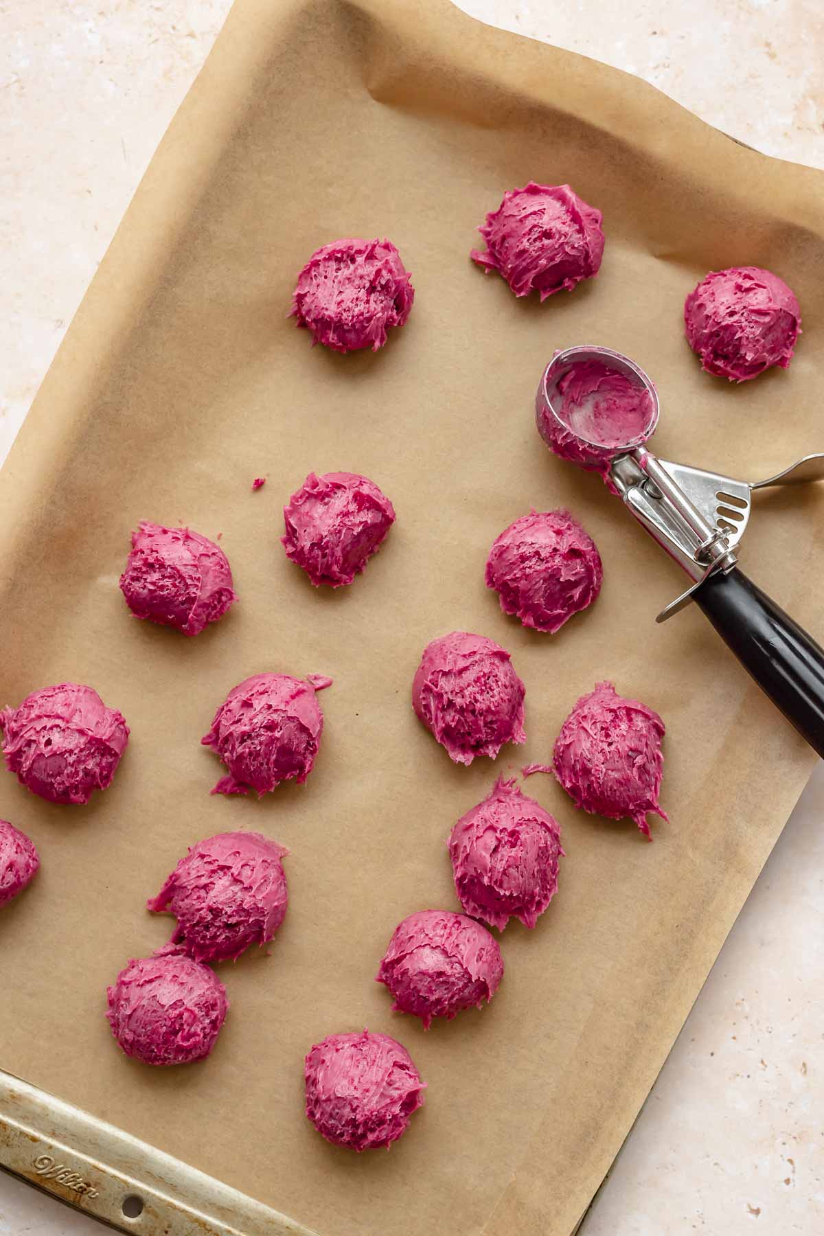 Balls of raspberry truffles on a sheet pan with parchment paper.