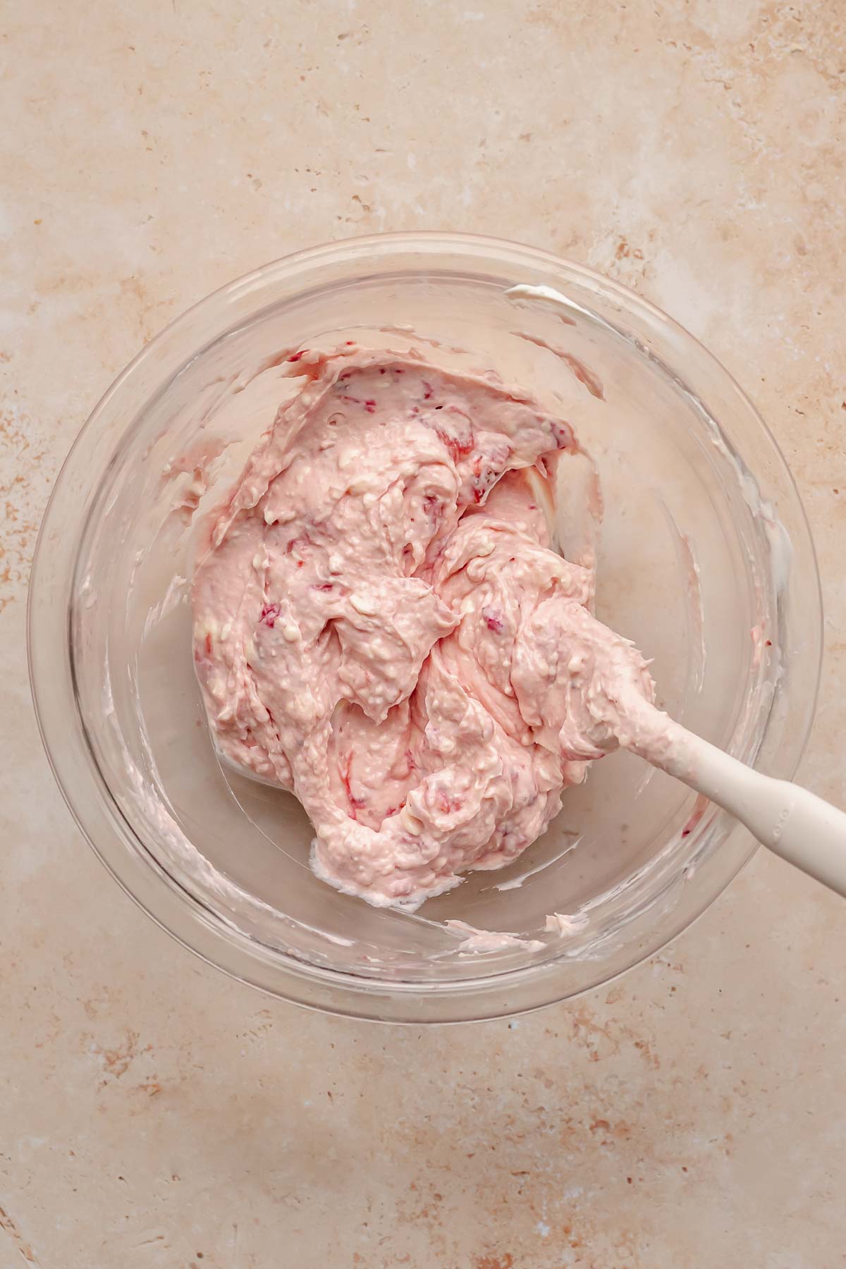 Strawberry syrup and cream cheese mixed together in a bowl with a spatula.